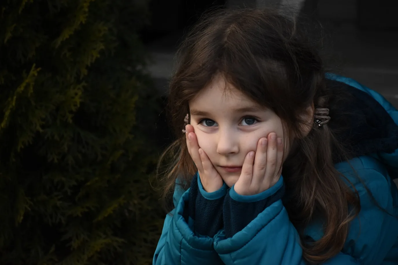 Mädchen in einer blauen Winterjacke stützt das Gesicht nachdenklich in beide Hände